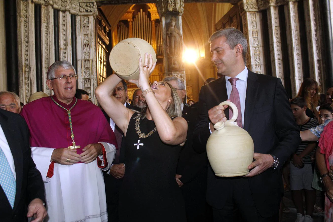 La alcaldesa levanta el botijo para beber en presencia del arzobispo. 