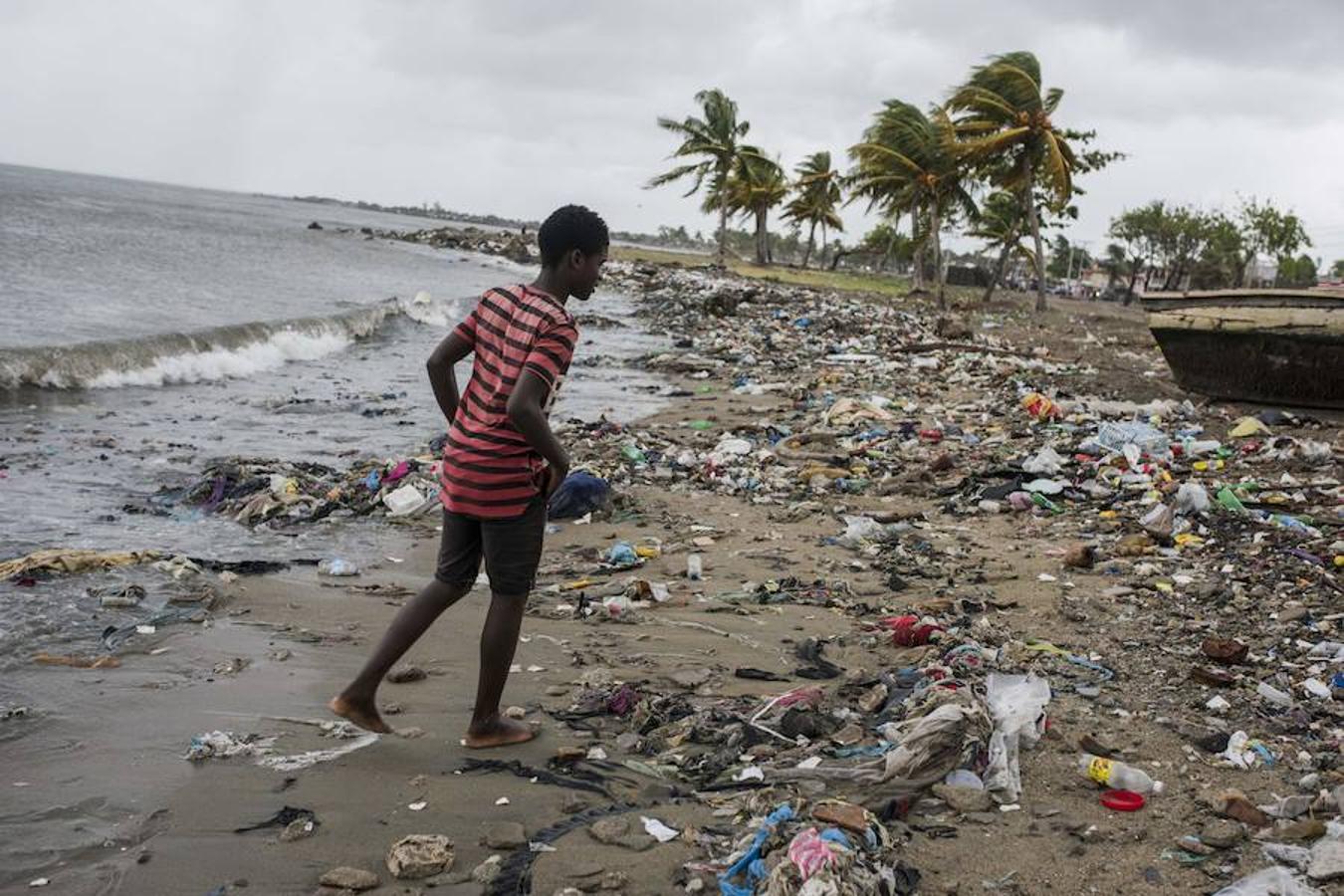 Un joven camina por la playa cubierta de desechos arrastrados por los fuertes vientos. 