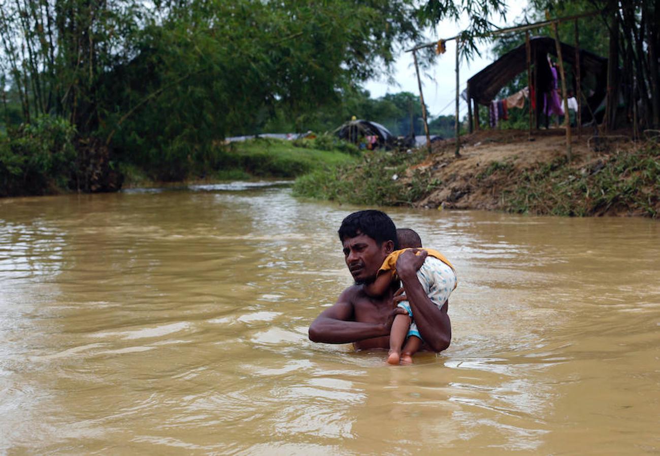 Un rohingya atraviesa una riada con un niño en brazos en un campo de refugiados de la ciudd bangladesí de Cox's Bazar.. 
