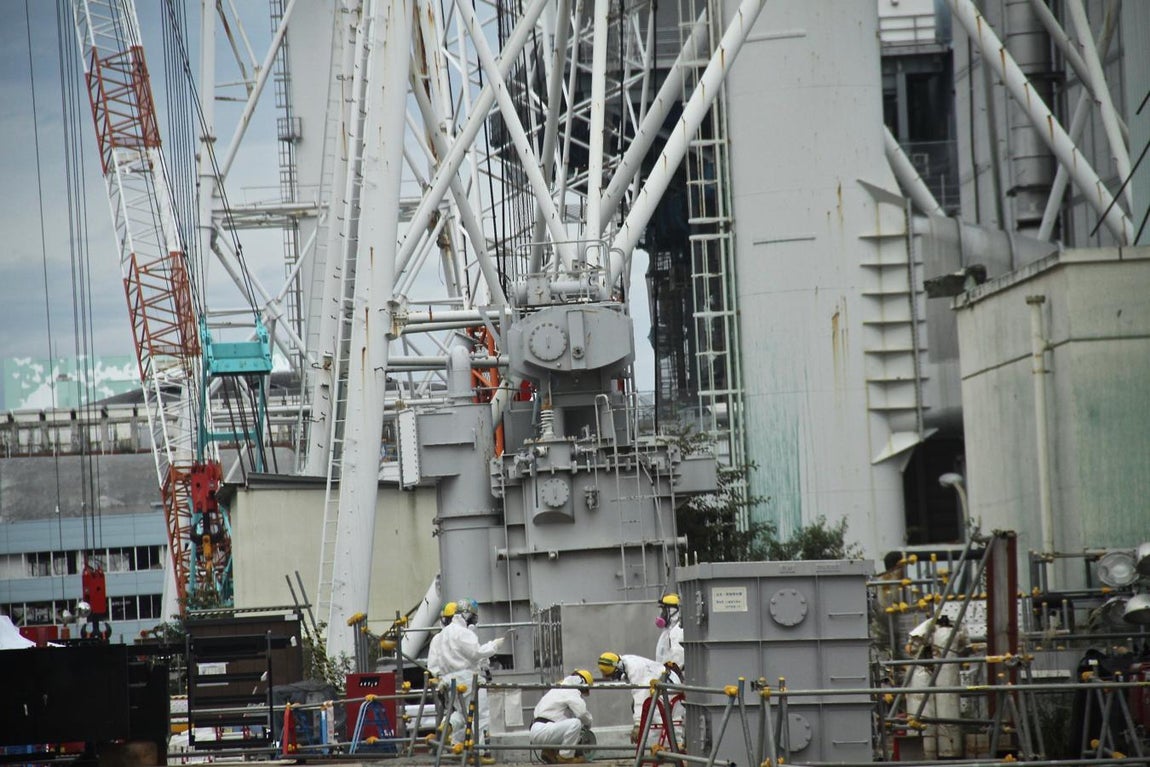 Protegiéndose con trajes especiales y máscaras contra la radiactividad, un grupo de operarios trabaja junto al edificio de un reactor. 