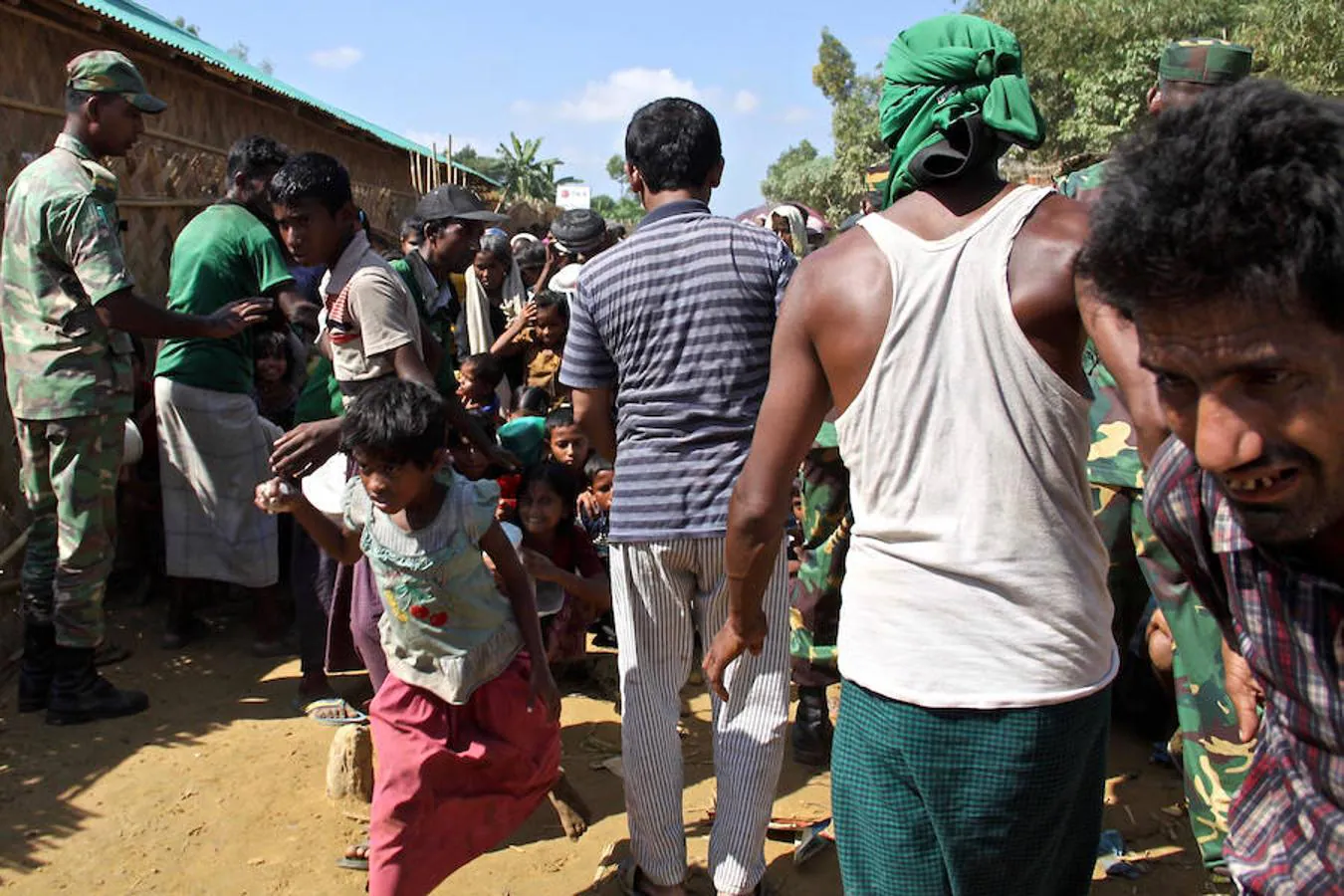 Con la mirada perdida como posesos, la multitud se abalanza desesperada sobre los puestos del reparto de comida mientras los soldados bangladesíes intentan contenerlos a palos con cañas de madera. 