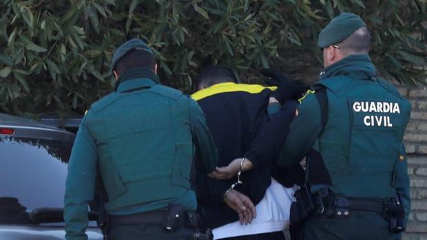 Dos guardias civiles trasladan hasta el vehículo a uno de los tres detenidos.