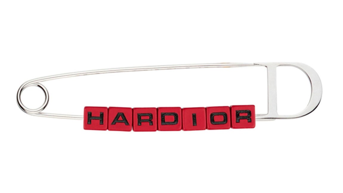 Dior. Imperdible metálico realizado con perlas cúbicas de aluminio lacado y escritura HARDIOR. (Precio: C.P.V.)