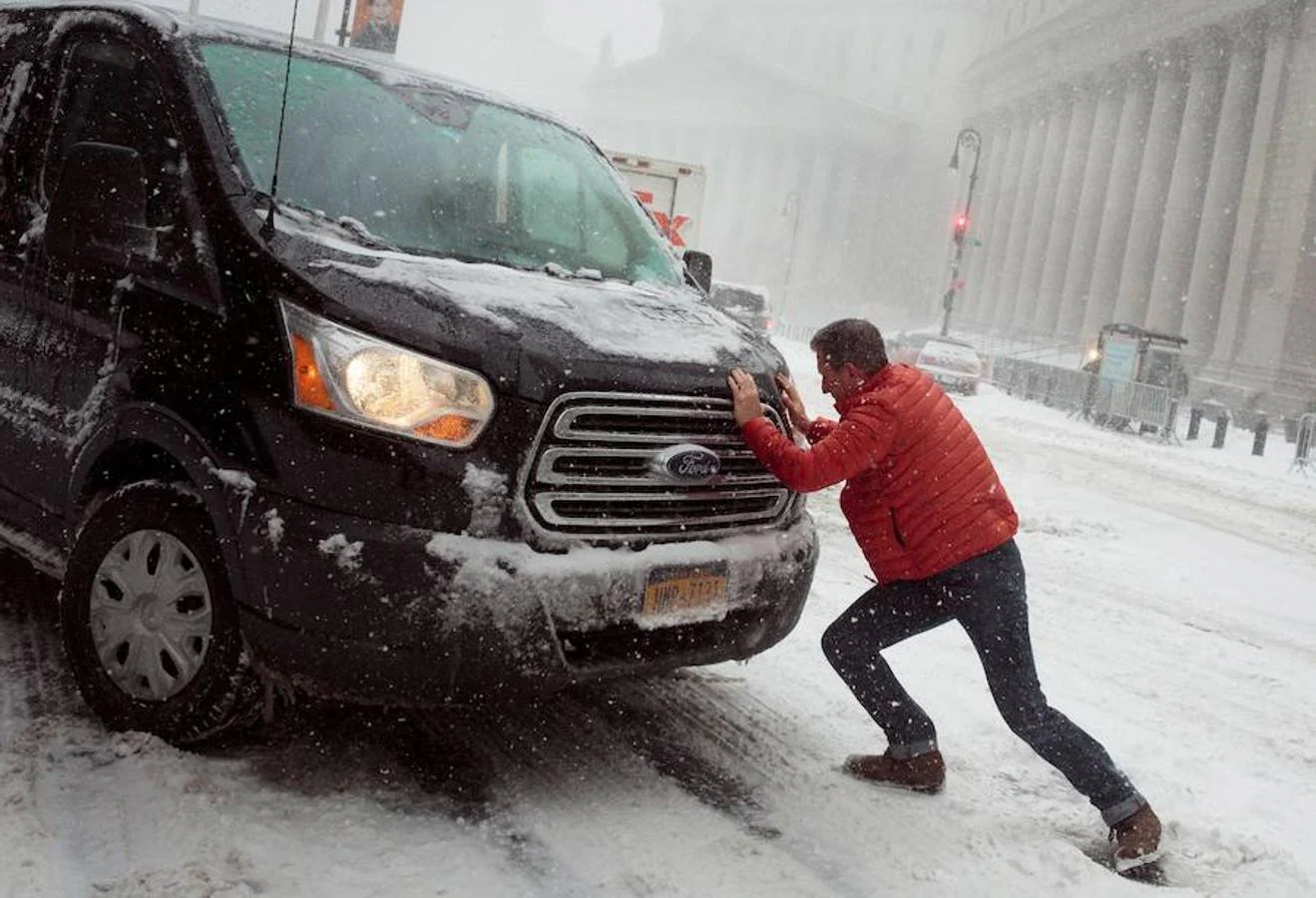 Un hombre empuja una furgoneta atascada en la nieve en el puente de Brooklyn.. 