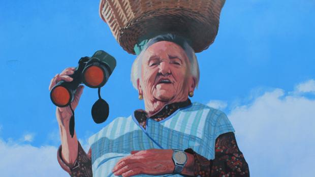 Lady Falcón. «Noventa y cinco años de buen humor», dice Yoseba MP sobre Carmen. Su marido, explica el pintor, trabajaba en la casa de la depuradora de agua que daba servicio a las viviendas de los trabajadores de fabrica de As Pontes de García Rodriguez (La Coruña), antes de la llegada de Endesa al pueblo. Con la jubilación del marido se tuvieron que mudar de casa y compraron un piso enfrente de la depuradora. Carmen, cuenta Yoseba MP, lleva más de veinte años de viuda viviendo sola y de forma autosificiente. «Es muy habladora, me invité a comer a su casa cuando terminé el mural. No me dejó levantarme de la mesa, todo lo hacía ella, despacio pero con ritmo. Me limité a escuchar la historia de su vida comiendo su tortilla: mucho trabajo y mucha pobreza hasta que llegó el trabajo de la depuradora. Como homenaje al nombre por el que todo el pueblo la conoce, «Carmen da depuradora», la subí a un deposito de agua como los que coronan  muchas viviendas del rural, y le puse unos prismáticos. As Pontes es tierra de setas y «Lady Falcón» busca llenar su cesto de amanitas muscarias», señala Yoseba MP sobre este trabajo.