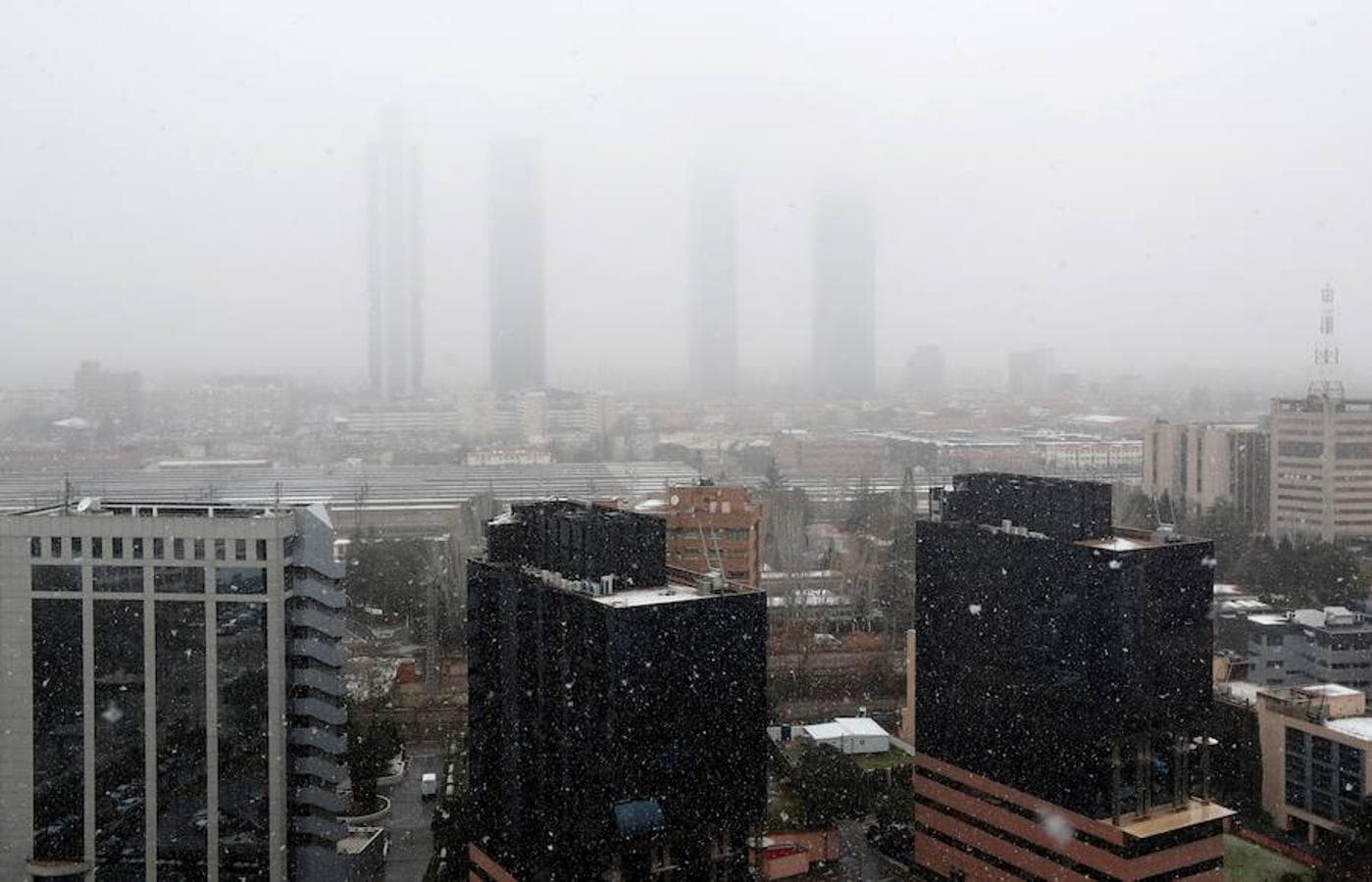 La nieve en Madrid ha empezado tímida y cayendo sobre mojado, pero a media mañana ha conseguido cuajar sobre vehículos y jardines. Vista del distrito financiero Cuatro Torres Business Area. 