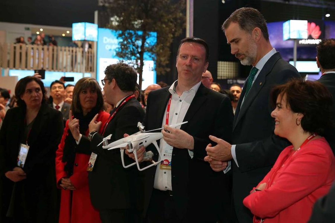El Rey Felipe VI atiende las explicaciones del directivo del GSMA, Michael O`Hara, junto a la vicepresidenta del Gobierno, Soraya Saénz de Santamaria. 
