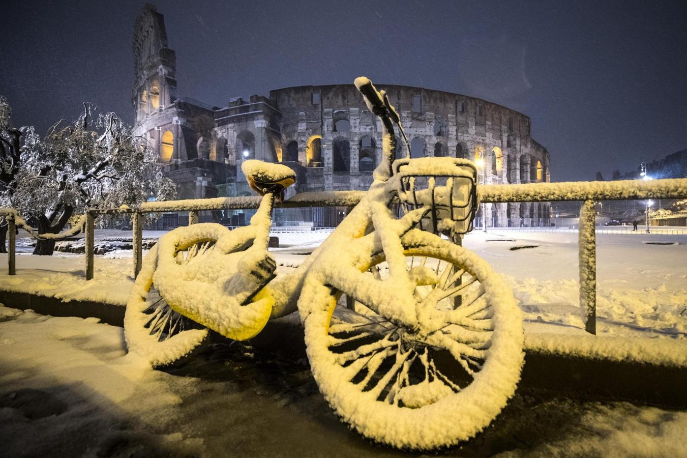 Una bicicleta cubierta completamente por la nieve con el Coliseo de fondo, en Roma. 