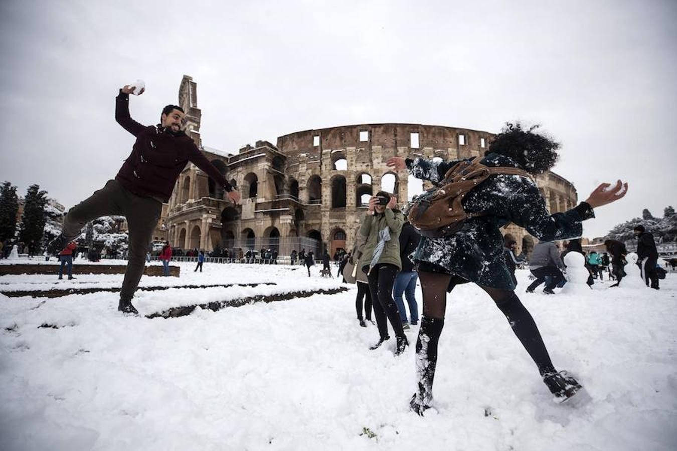 Turistas y viandantes juegan a tirarse nieve frente al Coliseo. 