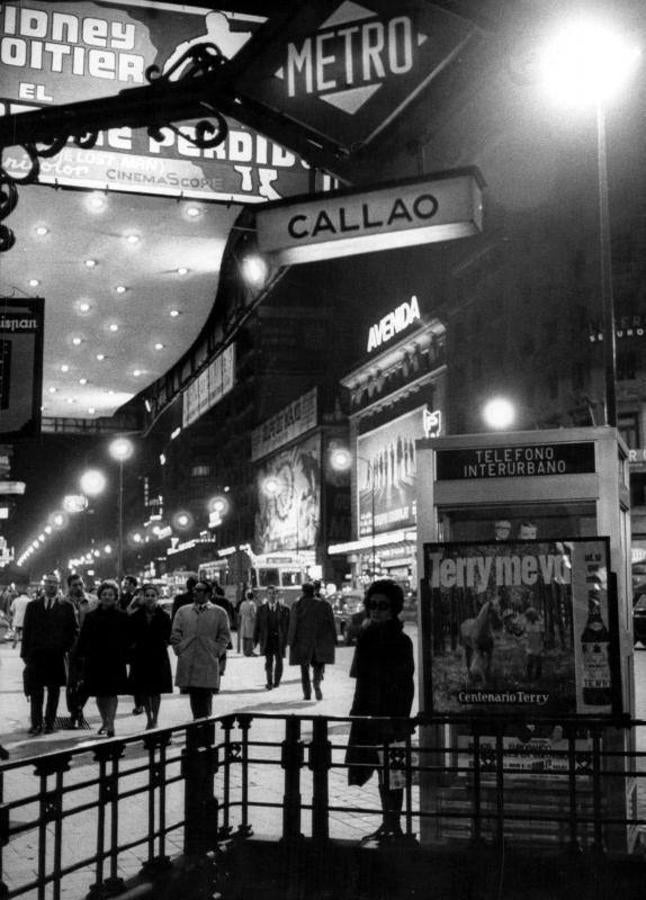 Madrid no se entiende sin Callao y su Broadway particular. En una vista parcial de la plaza conlindante con Gran Vía, una mujer espera en una extinta cabina telefónica mientras los viandantes observan los carteles teatrales (1970). 