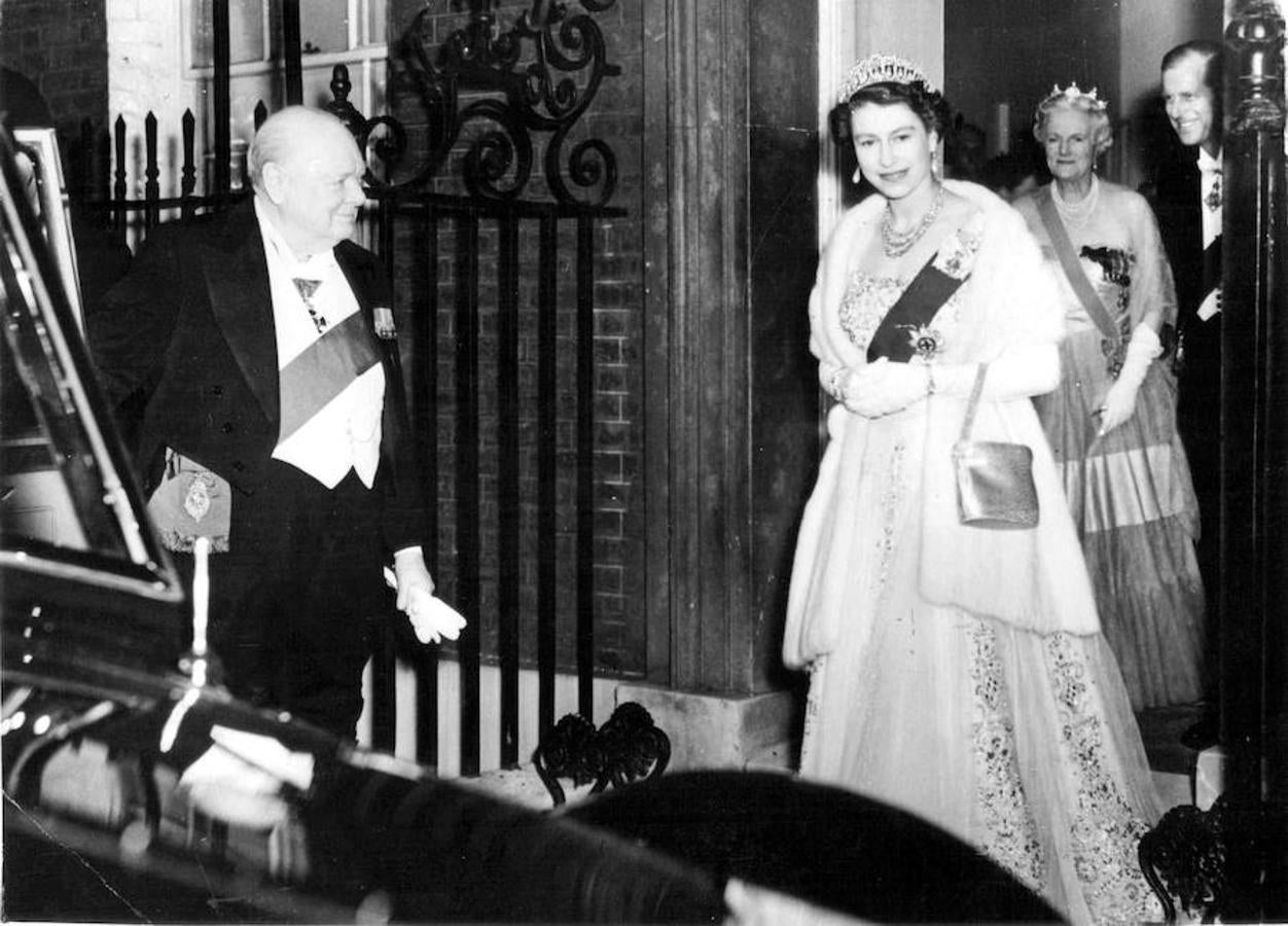 La Reina Isabel II de Inglaterra sale del nº 10 de Downing Street, dónde acudió a una comida ofrecida por el Primer Ministro, Winston Churchill, un día antes de su dimisión.. En la imagen, el primer ministro sujeta la puerta del coche de la soberana. Detrás puede verse al Duque de Edimburgo y a Lady Churchill