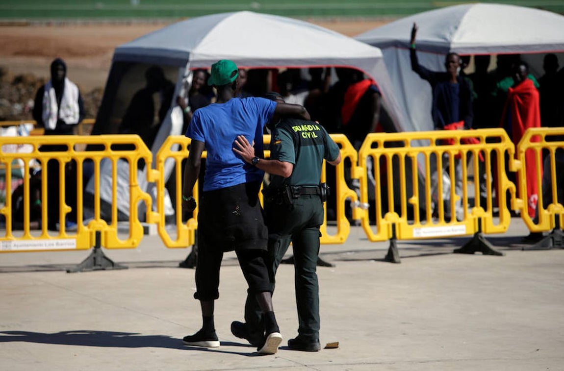 Un inmigrante rodea con el brazo a un guardia civil que cuida y vigila a las personas que llegan en patera a las costas de Cádiz y son trasladadas al pabellón «Antonio Gavira», en el municipio Los Barrios, cerca de Algeciras.. 