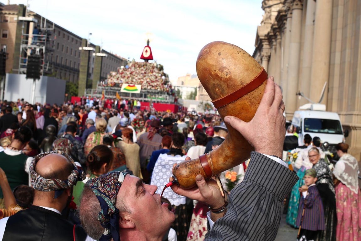 Un día de fiesta a lo grande. La Plaza del PIlar de Zaragoza se ha convertido en epicentro de la Hispanidad, un año más, en un ambiente de fiesta desbordante. En la imagen, un baturro hace un alto en el camino y toma un trago de vino, con la Virgen y su manto floral al fondo