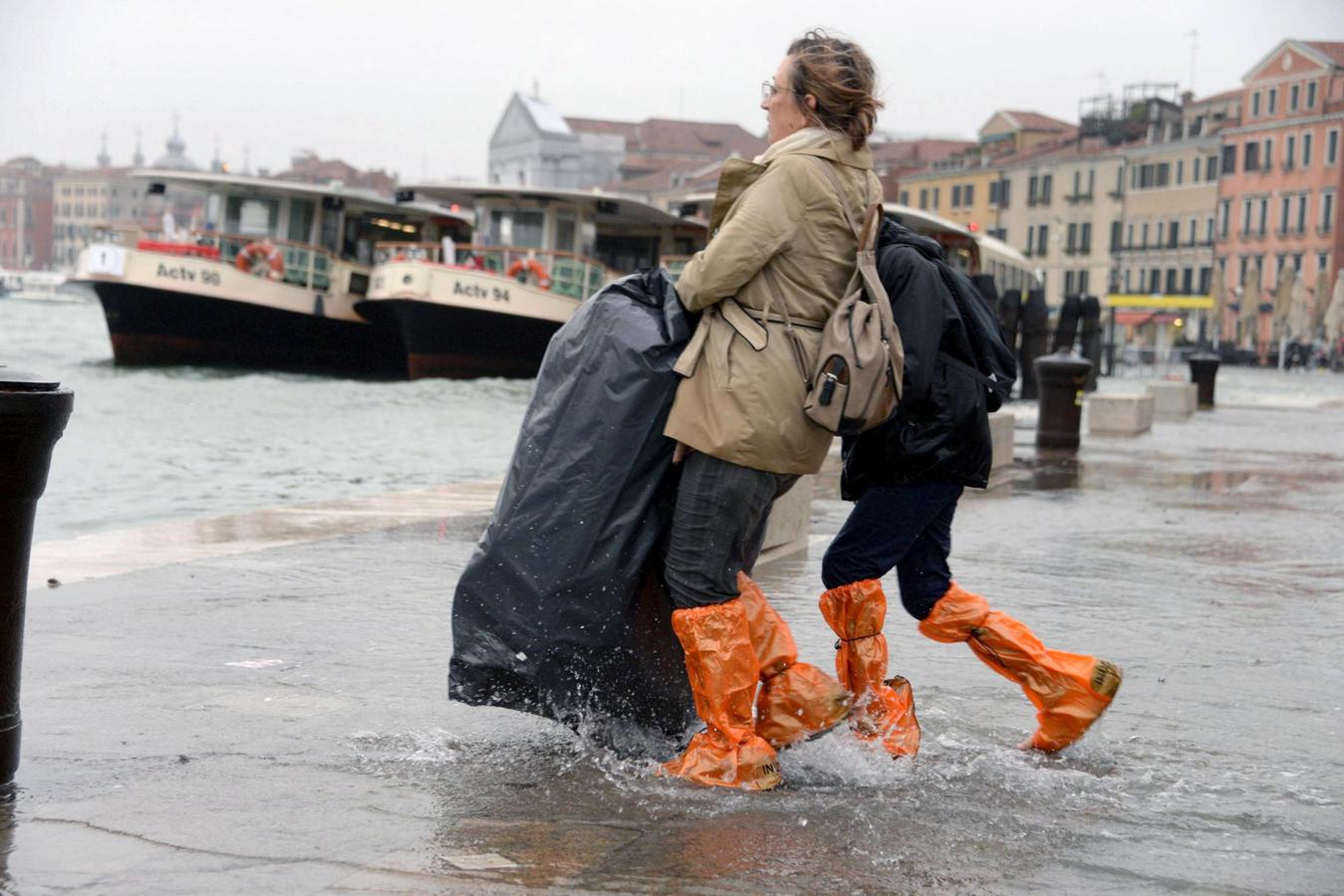 Dos turistas, con bolsas de plástico en los pies para aislarse del agua, caminan por una calle inundada en Venecia.. 