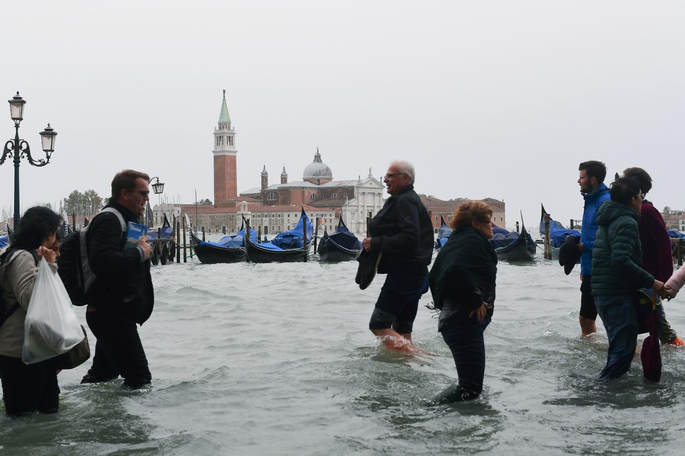 Algunos turistas, sorprendido por el «agua alta», han tenido que quitarse las zapatillas para cruzar las calles.. 