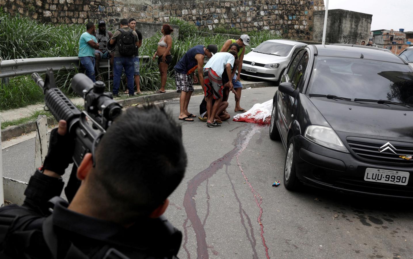 Un oficial de policía en primer plano mientras Fabiana Cardoso Domingues reacciona cerca del cuerpo de su hijo, Anderson Domingues, después de que fuera asesinado a tiros durante una operación contra bandas de narcotraficantes en el complejo de barrios marginales Alemao en Río de Janeiro (Brasil), el 1 de octubre de 2018.. 