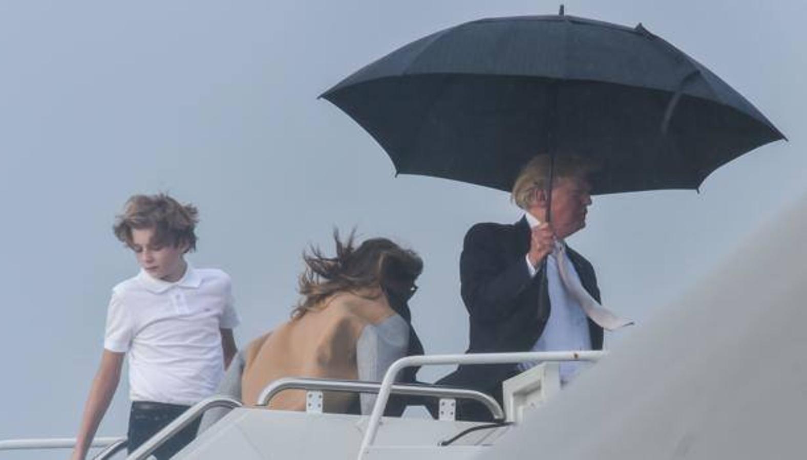 Donald Trump se tapa con un paraguas mientras su hijo y su mujer sufren las inclemencias del tiempo para subirse al Air Force One. 