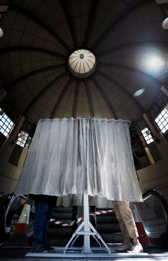 Dos ciudadanos ejercen su derecho a voto en una de las cabinas instaladas en el Mercado Principal de Alicante.. 