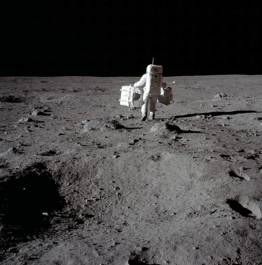 Buzz Aldrin con el Paquete de Experimentos Sísmicos Pasivos (en su mano izquierda) y el Retrorreflector de Rango Láser (en su derecha), en una foto tomada por Armstrong. 