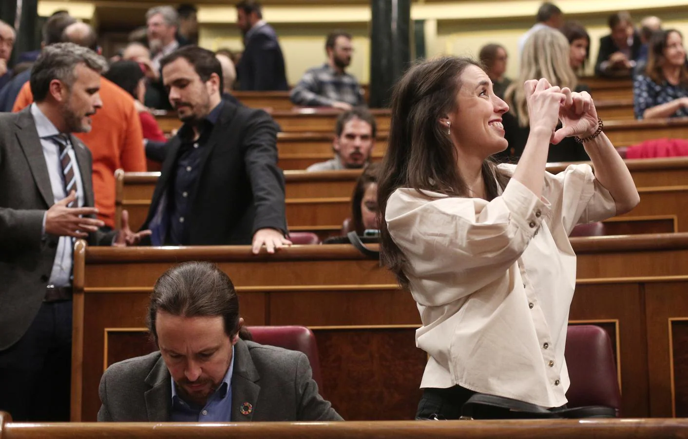 La portavoz de Unidas Podemos en el Congreso, Irene Montero, hace el signo de un corazón con las manos hacia alguien en la tribuna de invitados, junto al secretario general de Podemos, Pablo Iglesias, momentos antes de empezar la votación. 