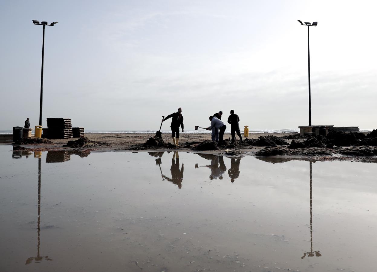 Operarios tratan de eliminar el barro y los charcos de agua que las tormentas han formado en la playa de las Arenas (Valencia)