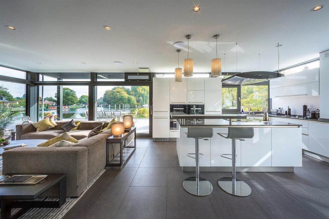 Diáfana. El salón principal y la cocina ocupan toda la planta baja y la separación entre ambos espacios es solamente un juego visual de su mobiliario y su decoración. En dominan los tonos oscuros y el cristal mientras que de la cocina se apodera el blanco. Los electrodomésticos y los muebles de almacenaje son minimalistas y en el centro del espacio hay una isla central práctica, estética y funcional