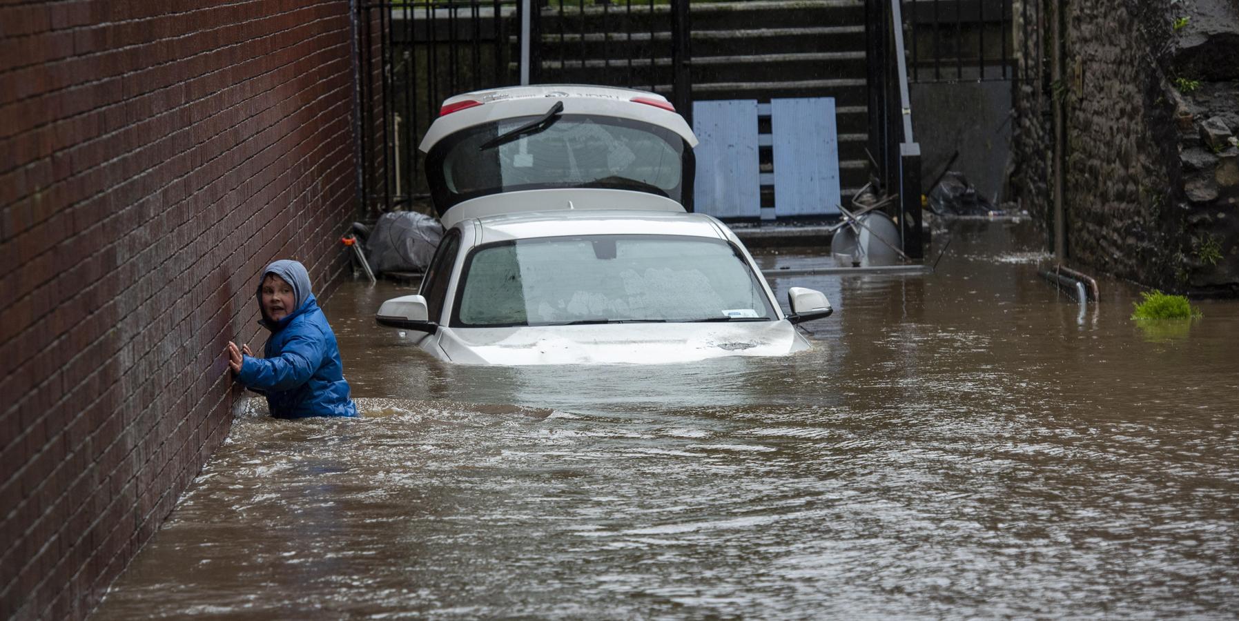 Un joven de la ciudad de Pontypridd, asustado, se apoya en la pared con el agua a la cintura junto a un coche prácticamente sepultado a causa de las inundaciones