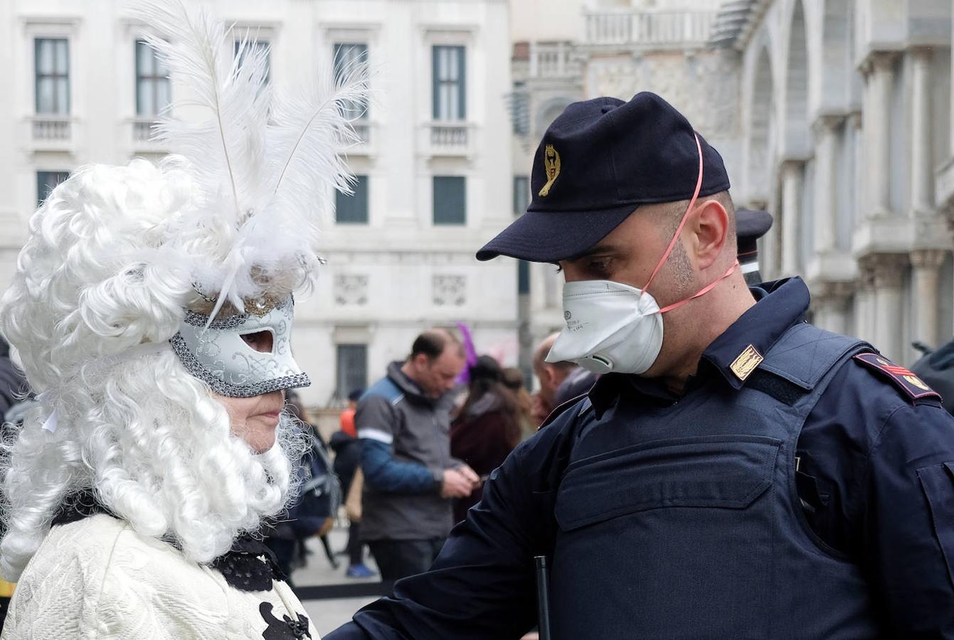 Un agente con una máscara protectora registra a una mujer disfrazada en Venecia. 