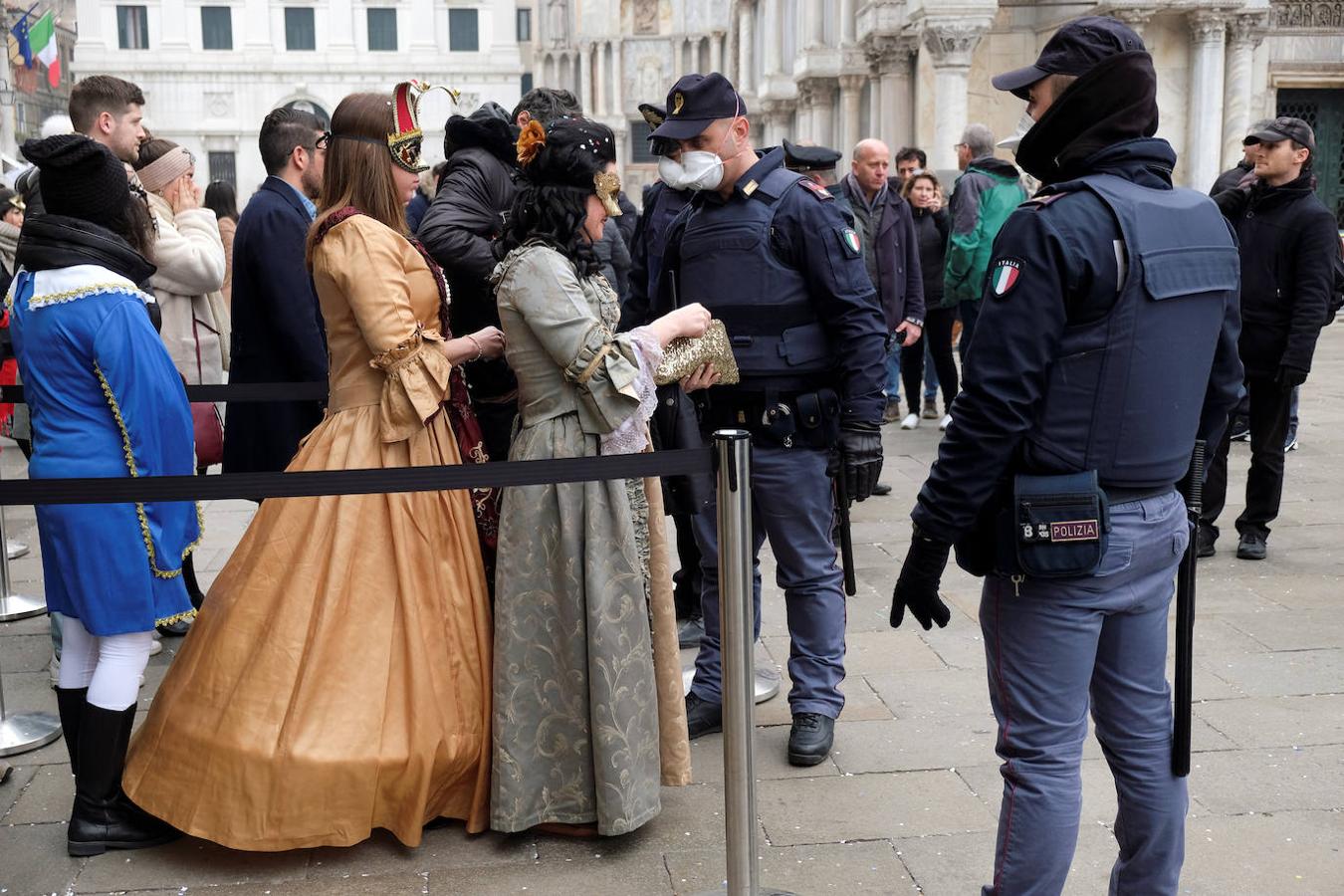 Dos mujeres disfrazadas muestran sus carteras a dos guardias que llevan mascarillas protectoras en Venecia. 