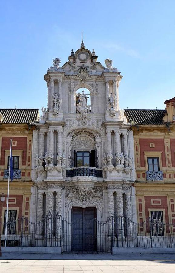 Palacio de San Telmo. El Palacio de San Telmo está situado en la Avenida de Roma y hoy en día acoge la sede de la Presidencia de la Junta de Andalucía. Anteriormente, funcionó como palacio real y como seminario. En su origen fue un colegio de marineros.Es un edificio barroco que se construye entre los siglos XVII y XVIII. Su fachada principal es una de las más famosas de la arquitectura churrigueresca. Fue realizada por Matías José de Figueroa entre 1.730 y 1.734, se compone de tres cuerpos La puerta de entrada cuenta con tres columnas por cada lado y un balcón sostenido por Atlantes. En el tercer cuerpo están las figuras de san Telmo, patrón de los navegantes, y a sus lados las de san Fernando y San Hermenegildo.El palacio es de planta rectangular y posee varios patios interiores, uno de ellos central, rodeado de jardines y estanques, con torres en las cuatro esquinas. De puertas para dentro, destaca el salón de Baile y la escalera principal.La fachada del edificio suele iluminarse con los colores de la bandera regional en los días previos al 28 de febrero, día de la Comunidad de Andalucía.