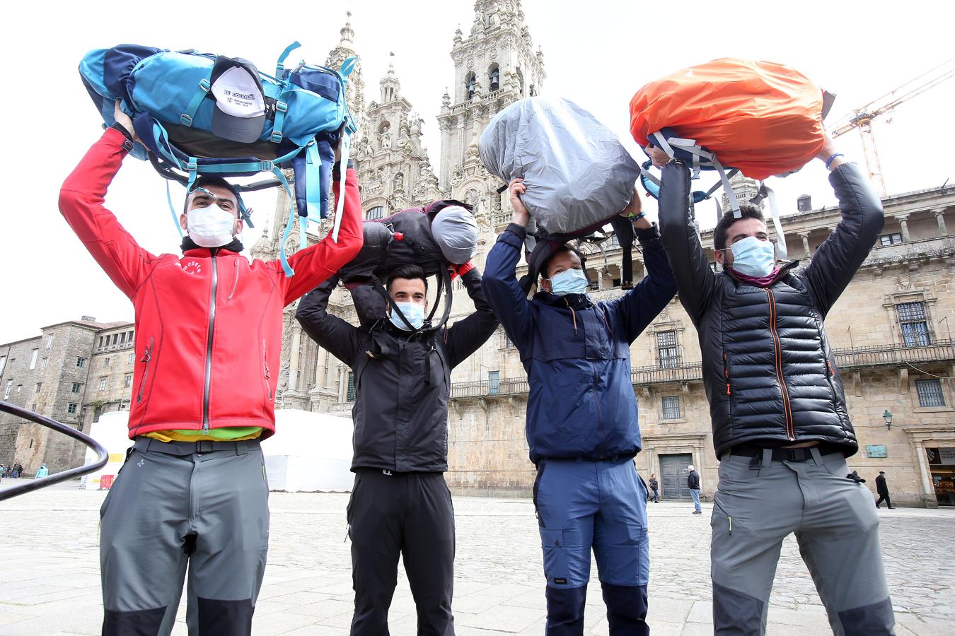 Cuatro peregrinos con mascarilla celebran su llegada a la Catedral de Santiago.. 