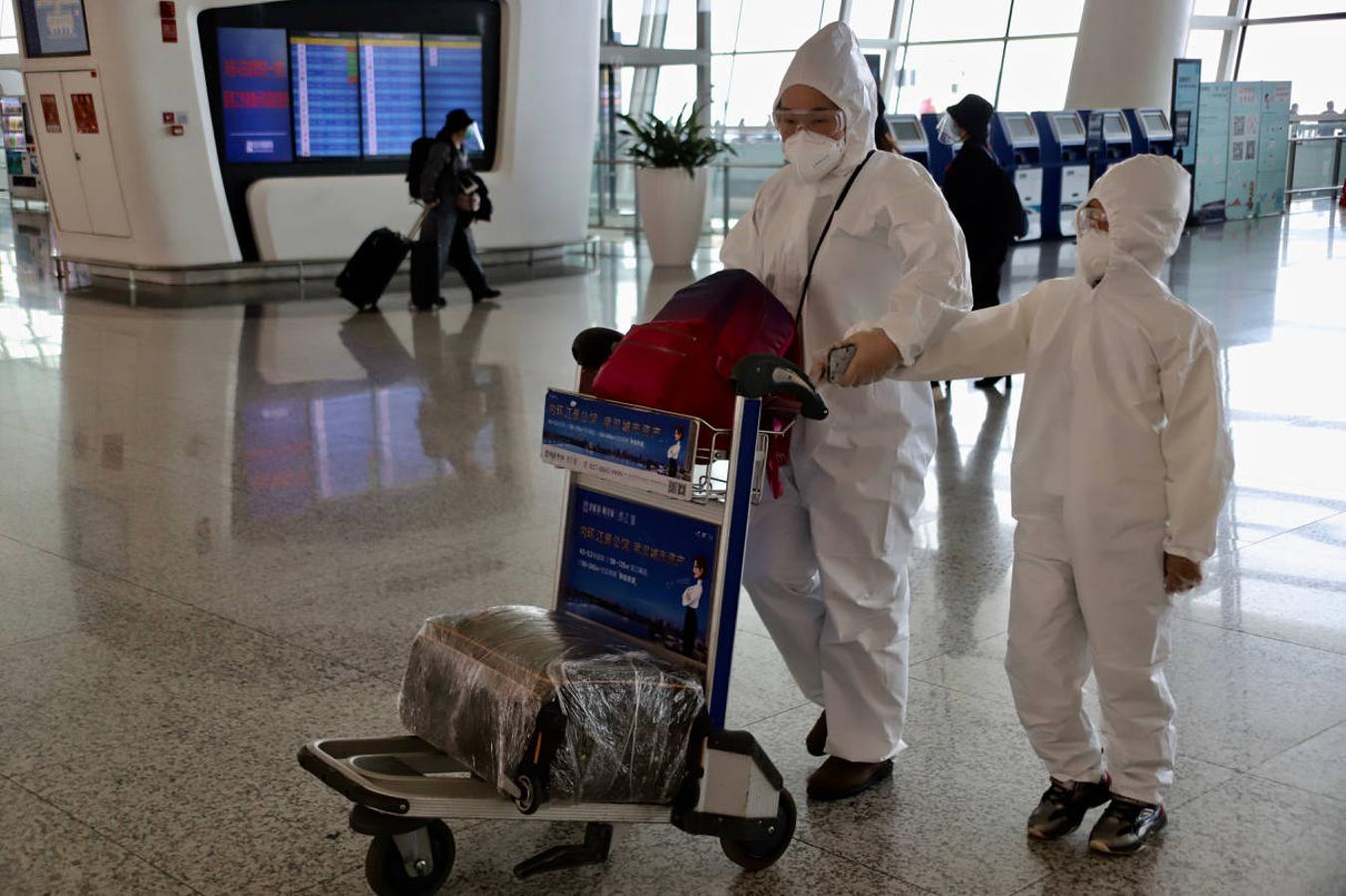 Una madre y su hijo se protegen con un mono especial y gafas para tomar un avión en el reabierto aeropuerto de Wuhan. 