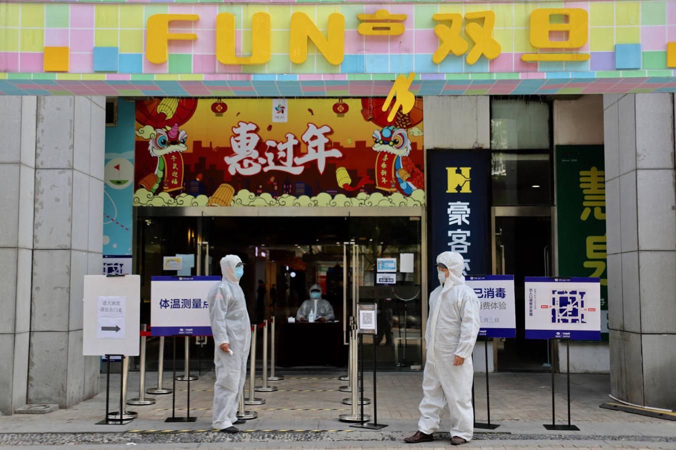 Vigilantes con monos blancos de protección controlan la temperatura en la entrada a un centro comercial de Wuhan. 