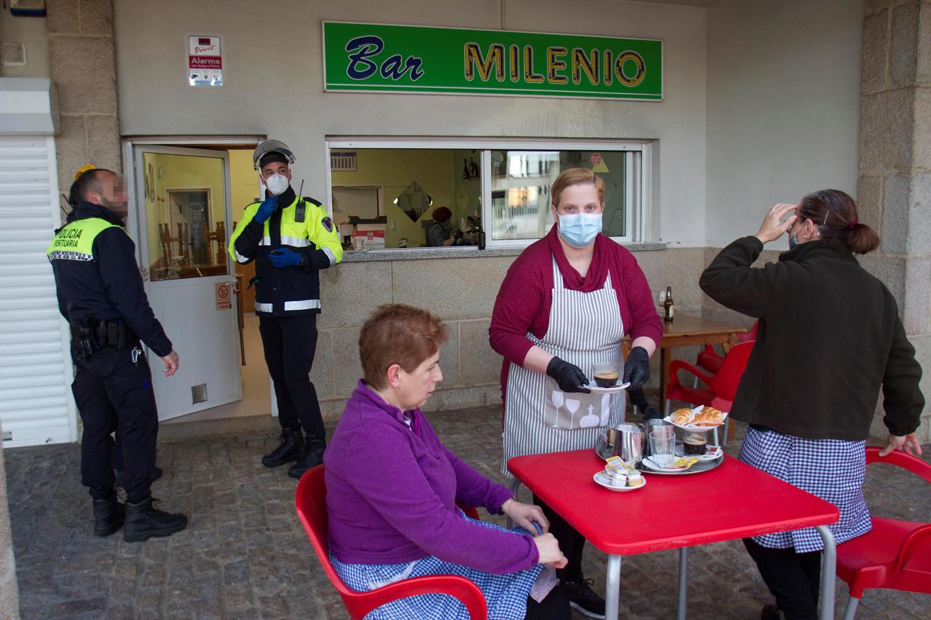 El placer de desayunar al aire libre. Las terrazas de los bares también están disponibles para el público al 50% de su capacidad. En la imagen, dos mujeres desayunan en un bar de Vigo, mientras dos agentes de la Policía portuaria esperan su turno. El servicio en el interior de los establecimientos esta prohibido