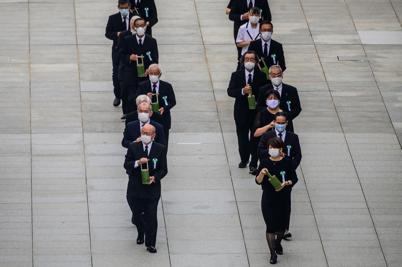 Un grupo de personas lleva pequeños jarrones con agua durante el acto en memoria de las víctimas de Hiroshima. 