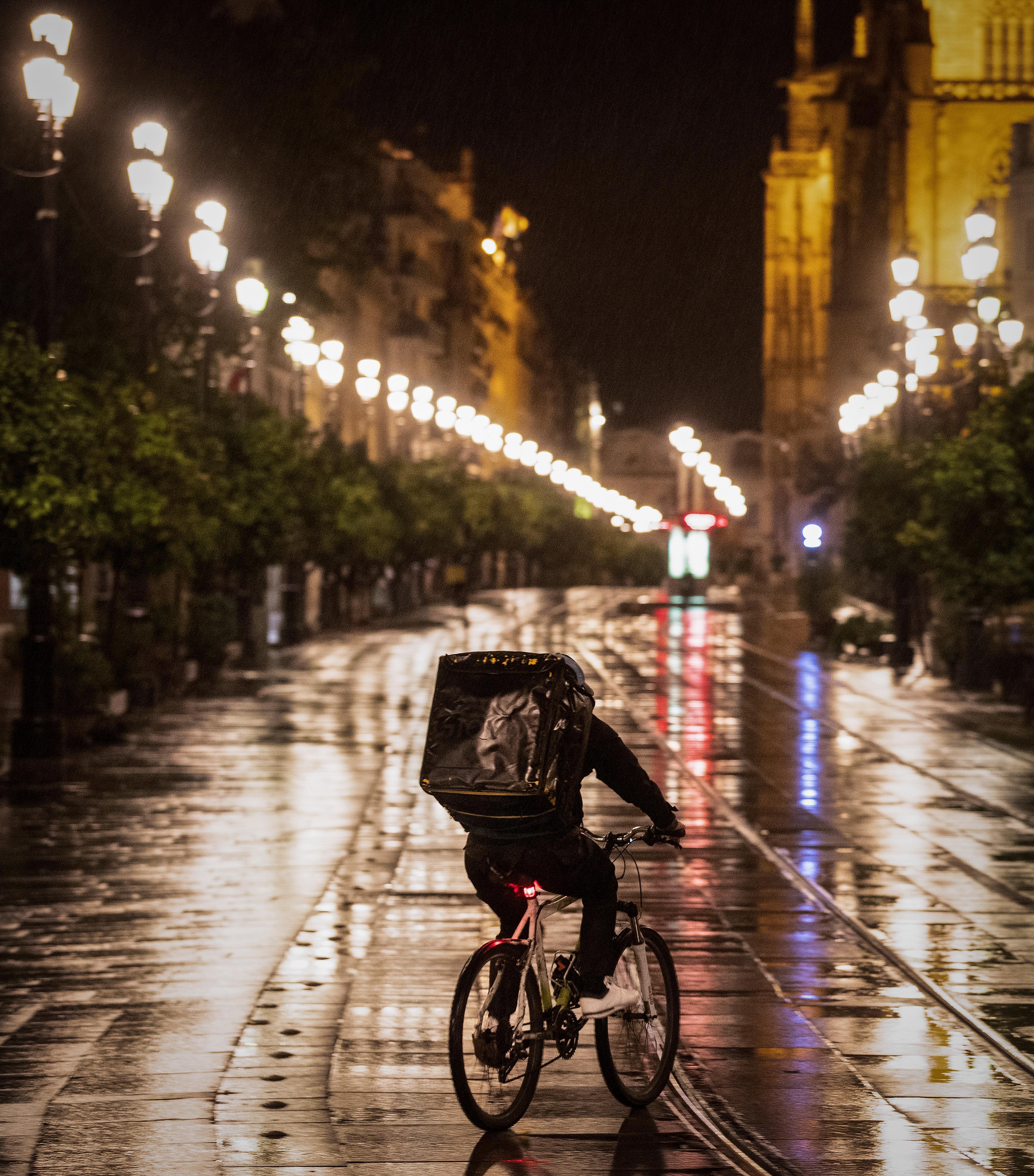 Reparto de comida a domicilio en Sevilla. La limitación a la movilidad nocturna tiene excepciones, como el ir y venir a trabajar, a hospitales o centros de salud. En la imagen, un repartidor de comida en su bici, camino de entregar un pedido en el caso antiguo de Sevilla