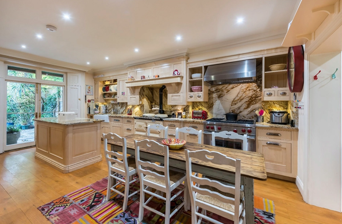 Así es el adosado de Ronnie Wood. La cocina, situada en un espacio semisubterráneo, destaca por sus muebles de madera con grandes tiradores metálicos, electrodomésticos de lujo, encimeras de granito claro, una isla con espacio extra de almacenaje y una mesa de comedor de estilo rústico.