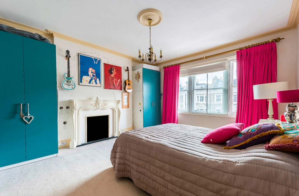 Así es el adosado de Ronnie Wood. En uno de los dormitorios se pueden ver armarios pintados en tonos turquesa y cortinas en tonos rosas, decoración que se completa con diferentes pinturas y guitarras, además de una majestuosa chimenea.