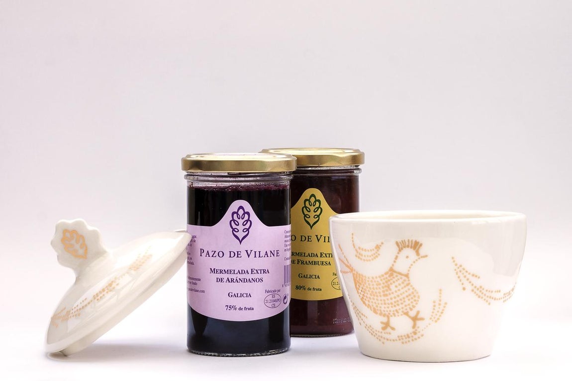 Mermelada artesanal. Se trata de un estuche compuesto por dos tarros de mermelada artesanal Pazo de Vilane, de frambuesa y de arándanos, junto con un tarro de loza blanca, realizado a mano por la firma de artesanía gallega “Mi madre no me deja”, perfecto para poner lamermelada. La pieza, pintada y decorada a mano en tonos blancos y dorado con la emblemática gallinita de Pazo de Vilane.Precio: 35€