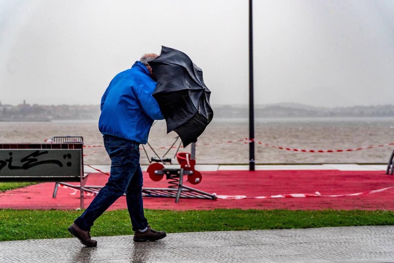 Vendaval en Santander. Un hombre sujeta con fuerza su paraguas mientras camina este lunes por la bahía de Santander. Cantabria permanece en alerta por fuertes vientos y oleaje debido a la borrasca «Bella»