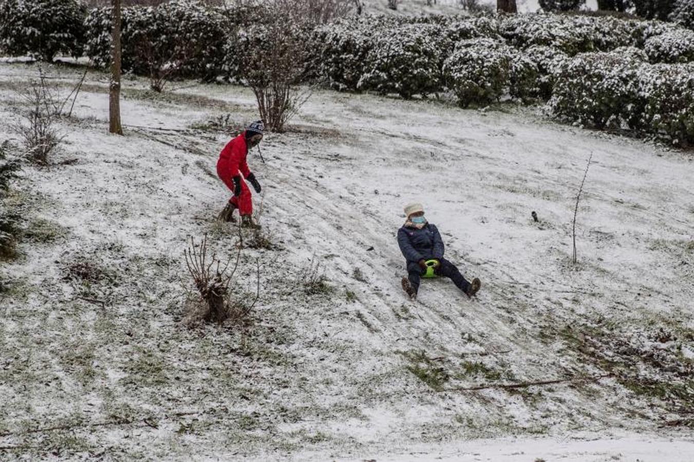 Dos personas aprovechan la nieve acumulada en un jardín para dejarse caer con una especie de trineo. 