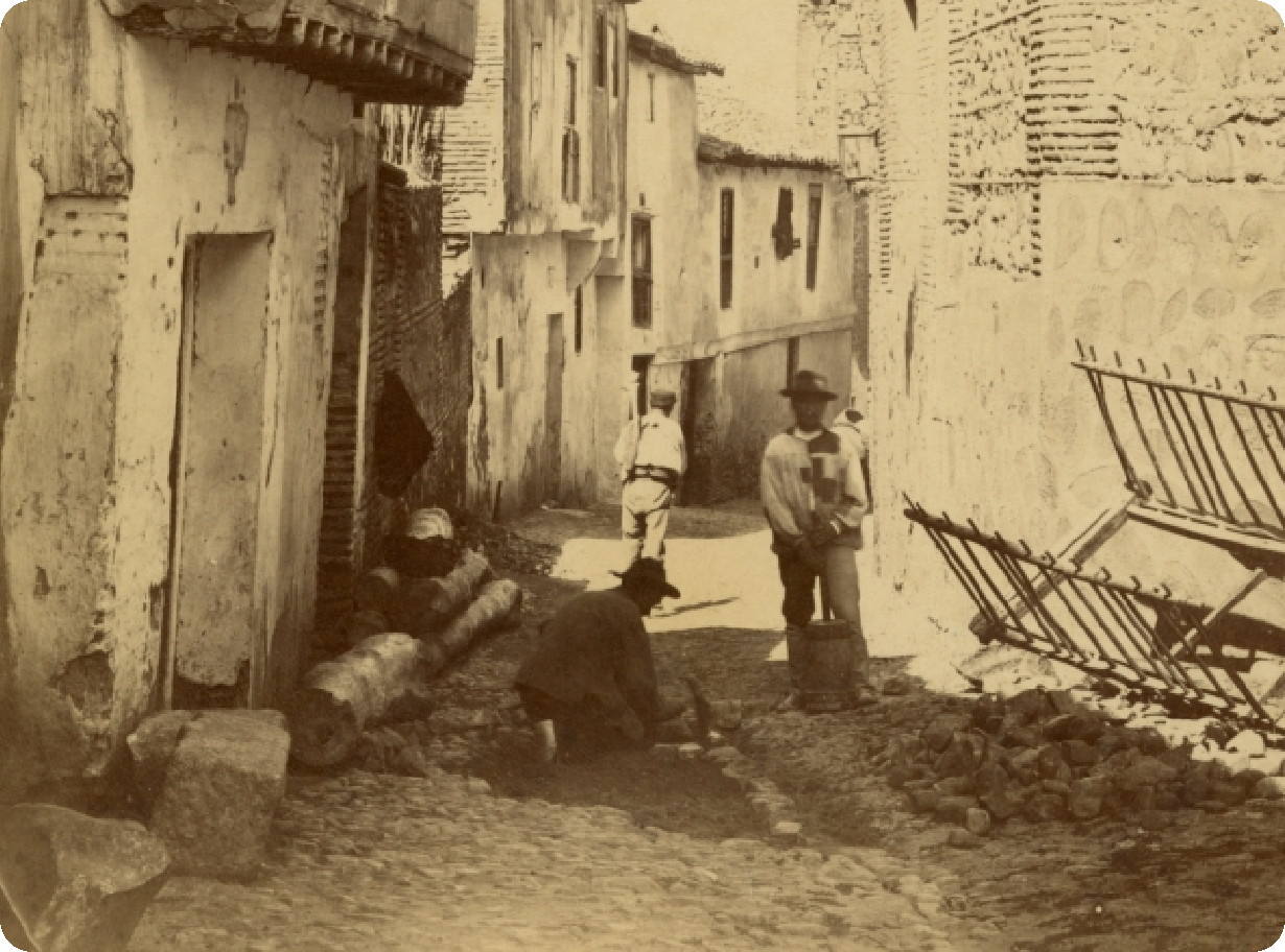 Dos empedradores trabajan con alcotana y pisón de mano, en la actual calle de Alfonso VI, hacia 1880. A la derecha, el muro de la iglesia parroquial de Santiago el Mayor. Fotografía de Casiano Alguacil. Archivo Municipal de Toledo. Colección Luis Alba. 