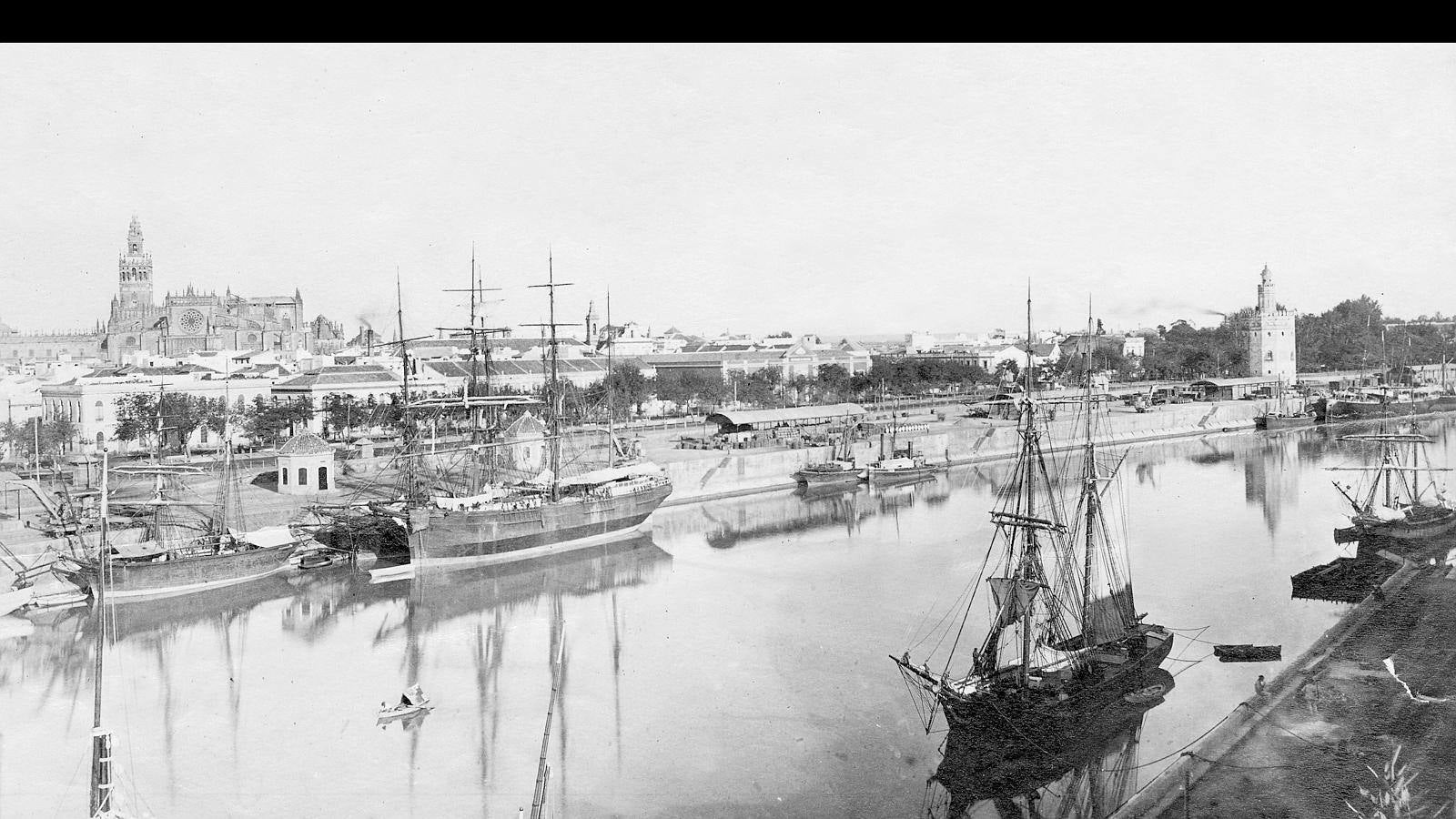 Panorámica de la ribera este del Guadalquivir, actual Paseo de Colón, flanqueada por la Catedral y la Torre del Oro, fechada hacia el 1900. Resultan llamativas las embarcaciones de vela que atracaban en la orilla en la época