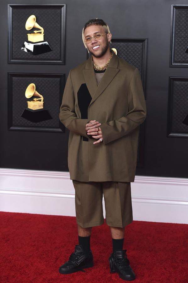 Jhay Cortez - Alfombra roja de los Grammy 2021. Su estilismo es la clara prueba de que el traje puede reinventarse hasta límites insospechados. Se decantó por un dos piezas color aceituna compuesto por unas bermudas y gran blazer de la marca 424. Lo conjuntó con dos grandes colgantes de oro de Martha Calvo.