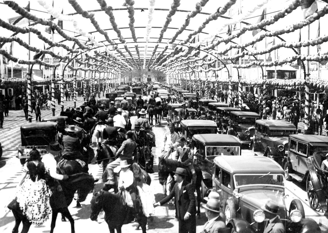Paseo de caballos en el que se permitían los vehículos de motor bajo los arcos de farolillos de la calle San Fernando, eje de acceso al recinto del Prado de San Sebastián, durante la Feria de Abril de Sevilla de 1924