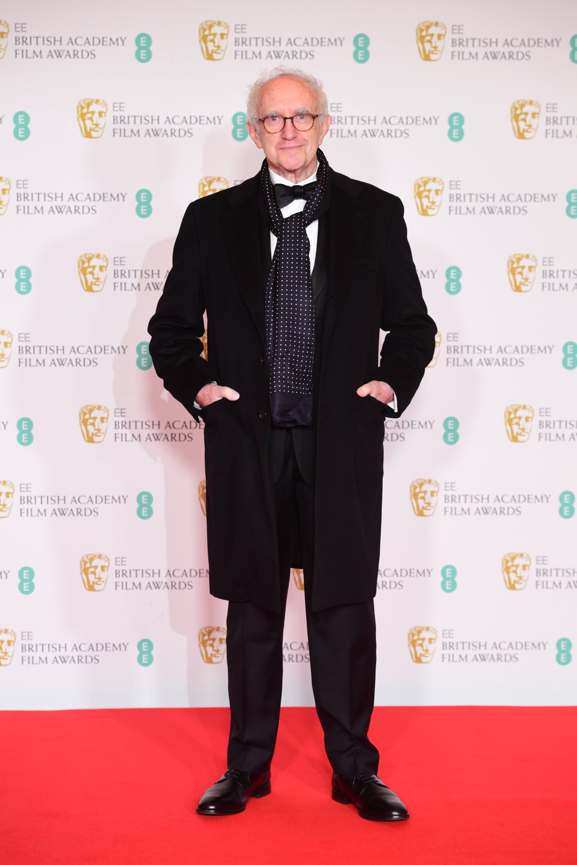 Jonathan Pryce – Los mejor vestidos de los BAFTA. Hizo de su elección una de las más elegantes simplemente añadiendo un fular de seda azul marino con topos sobre el abrigo.