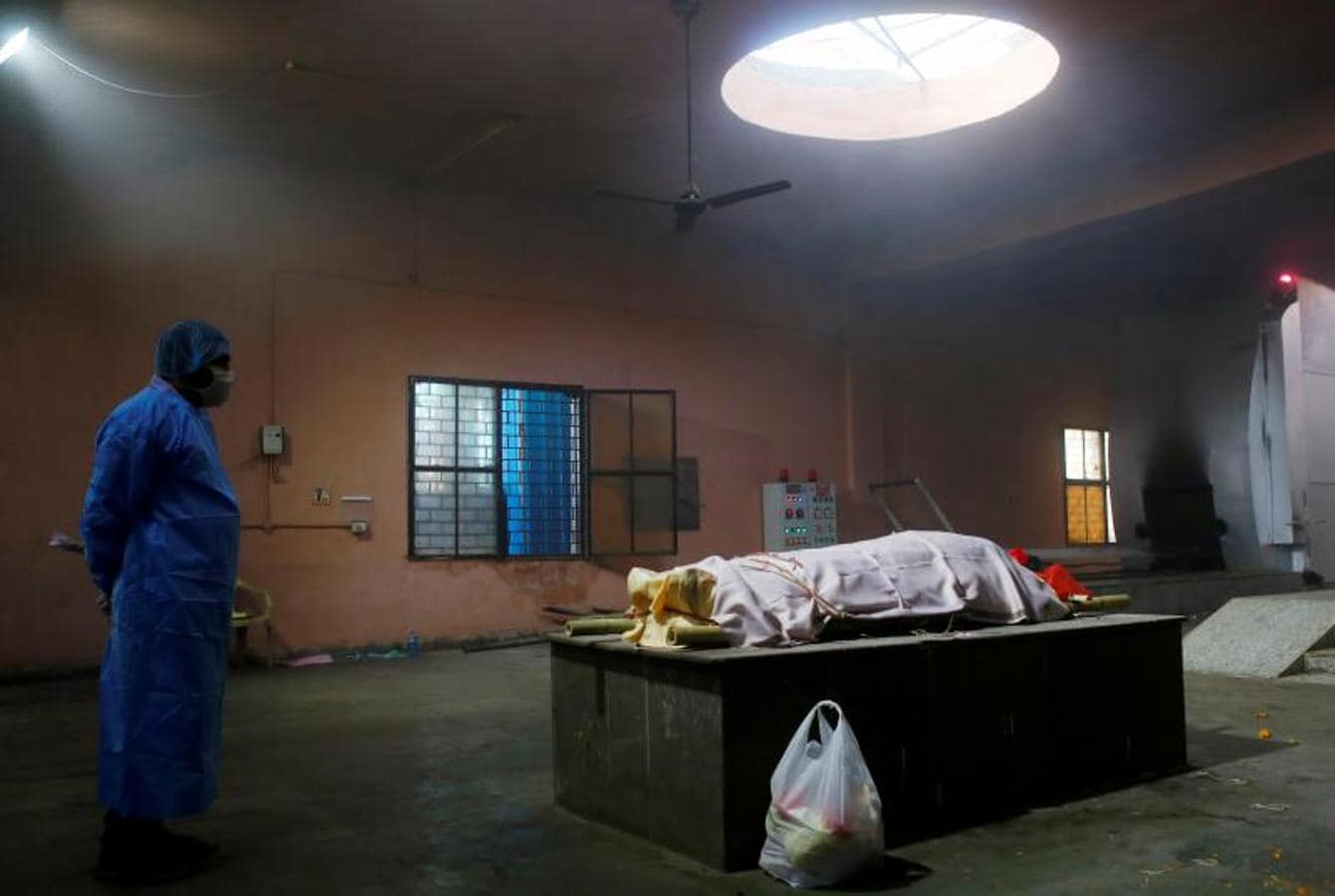 Un familiar con equipo de protección personal se encuentra junto al cuerpo de una mujer, que murió por Covid-19, antes de su cremación, en un crematorio en Nueva Delhi. 