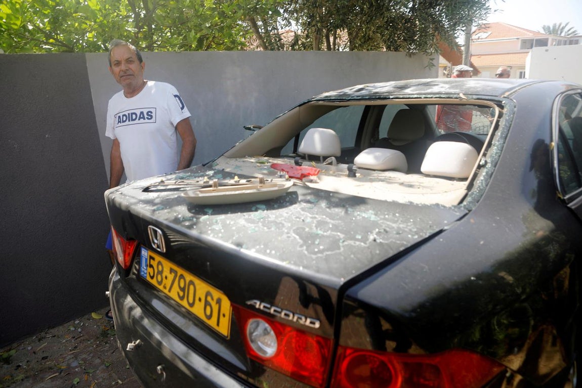 Un hombre junto a un coche dañado por el impacto del cohete. 