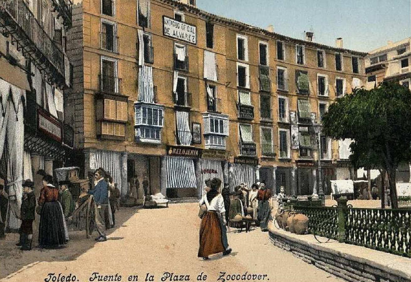 Fuente de Zocodover con la presencia de un organillero ante los soportales. Postal en tricromía por Purger &amp; Co., editada en 1903, con una escena plasmada en 1902. Archivo Municipal de Toledo. 