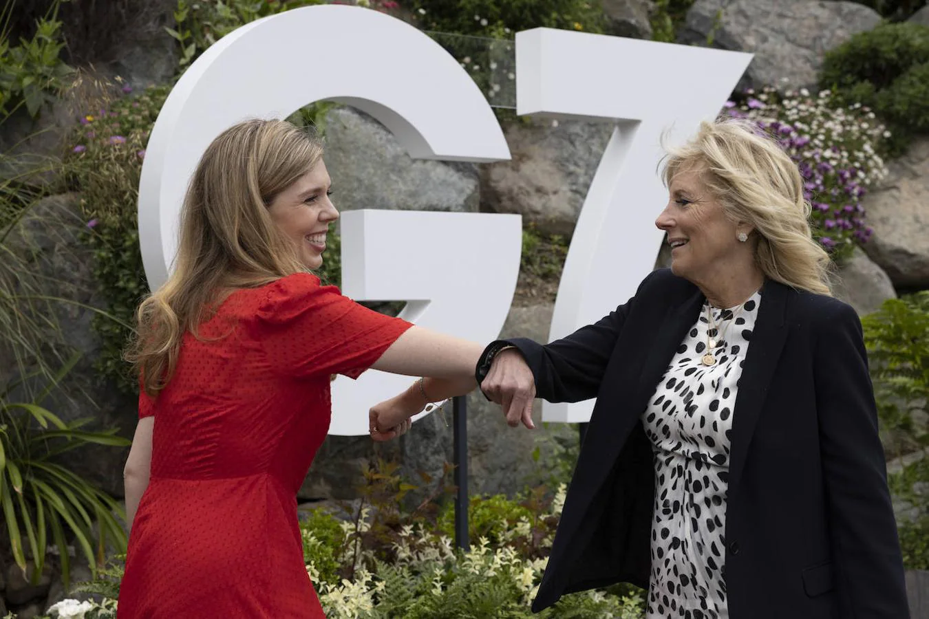 Carrie Johnson (i), esposa del Primer Ministro del Reino Unido, Boris Johnson, choca el codo con la Primera Dama estadounidense Jill Biden, frente al cartel del G-7. 